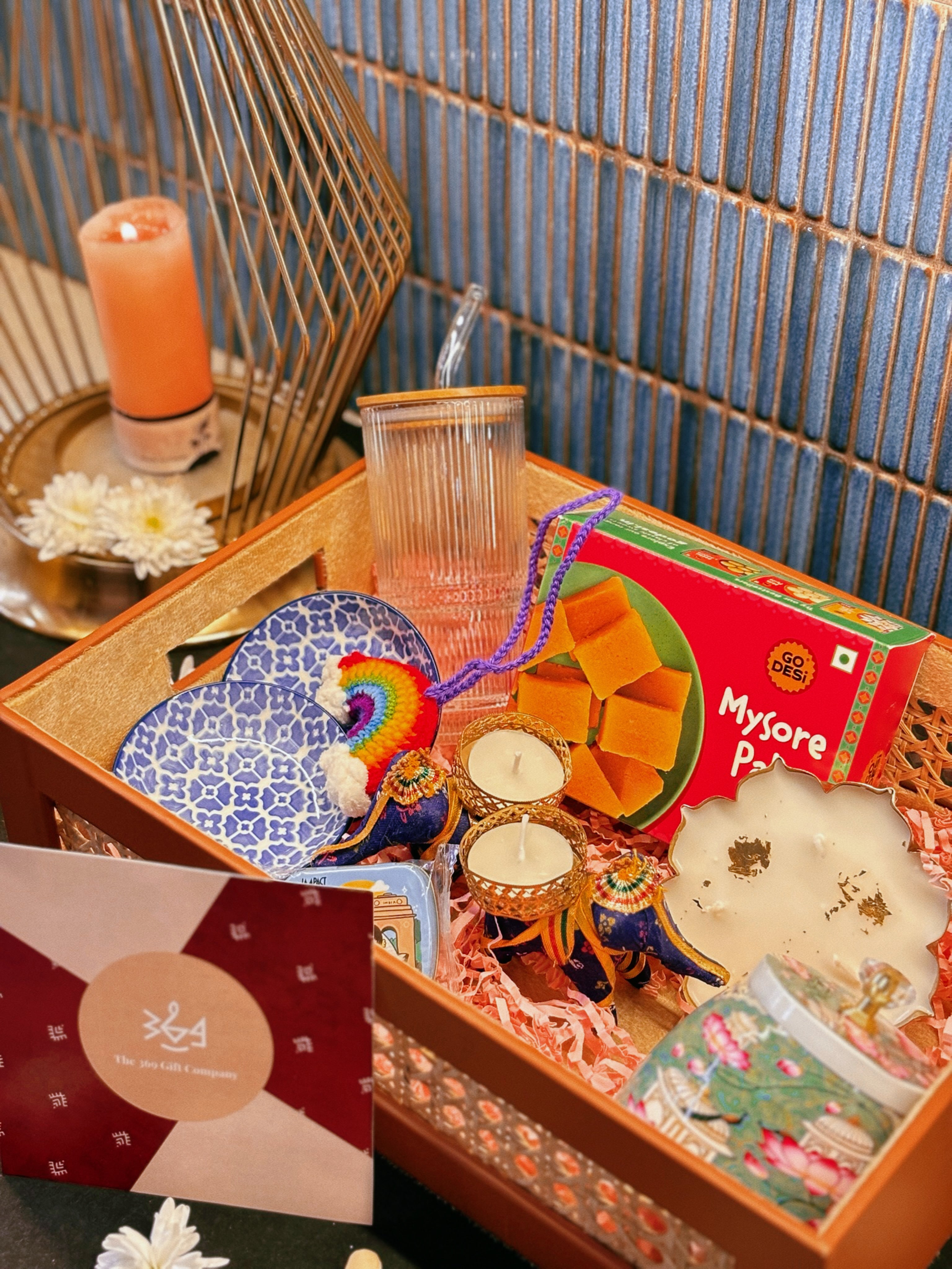 Luxury handcrafted wedding and event hamper by The 369 Gift Company — featuring a rattan tray with mocha leather detailing, Mysore pak, Urli Oudh candle, elephant tealight holders, nuts and seed-filled Pichwai metal jar, festive mints, rainbow crochet charm, starter bowls, and glass coffee tumbler — perfect for wedding favours, event gifting, and festive celebrations.
