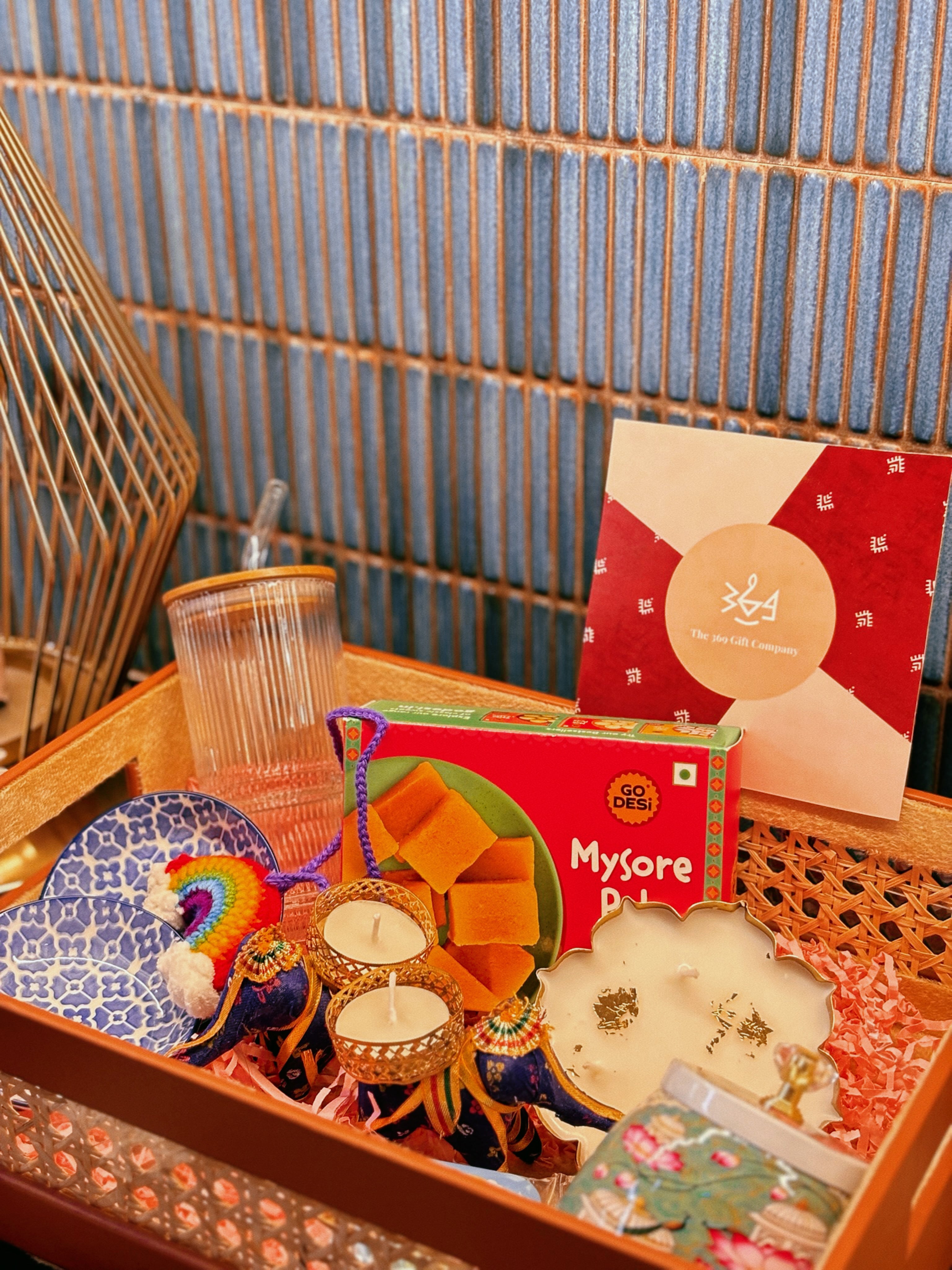 Luxury handcrafted wedding and event hamper by The 369 Gift Company — featuring a rattan tray with mocha leather detailing, Mysore pak, Urli Oudh candle, elephant tealight holders, nuts and seed-filled Pichwai metal jar, festive mints, rainbow crochet charm, starter bowls, and glass coffee tumbler — perfect for wedding favours, event gifting, and festive celebrations.